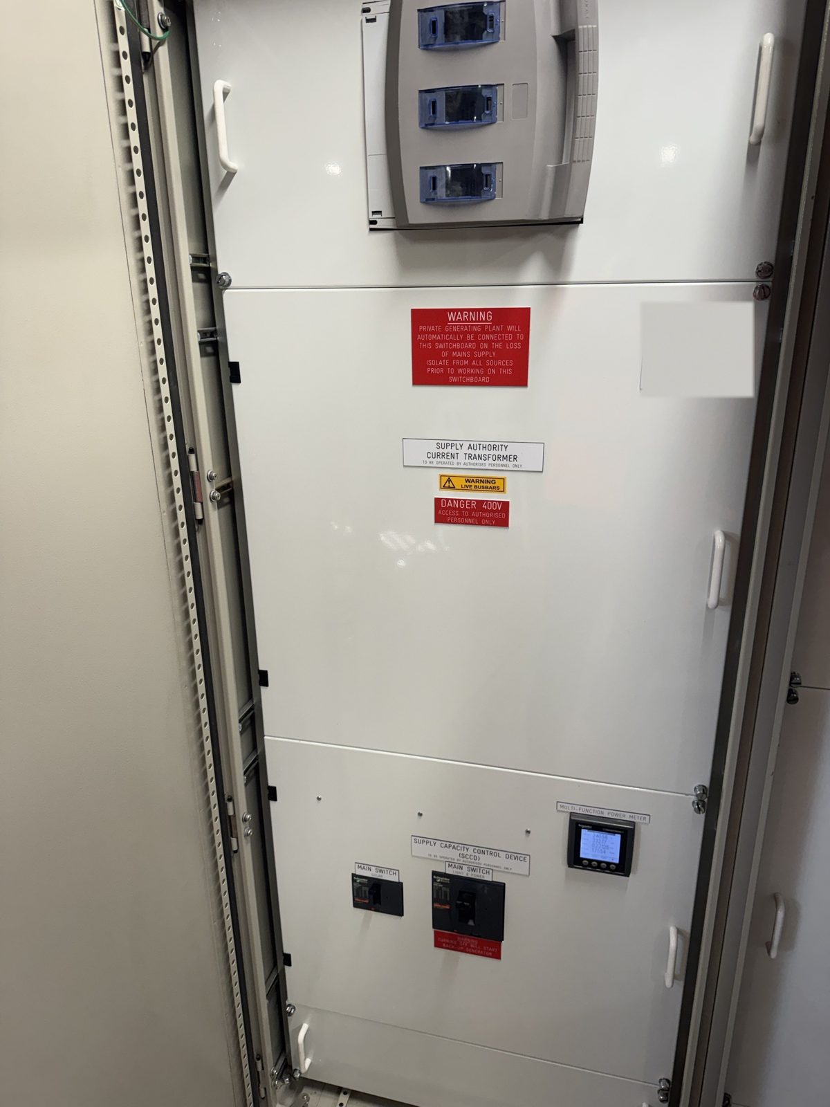 Main switch and metering section of a commercial switchboard with live busbar warning labels