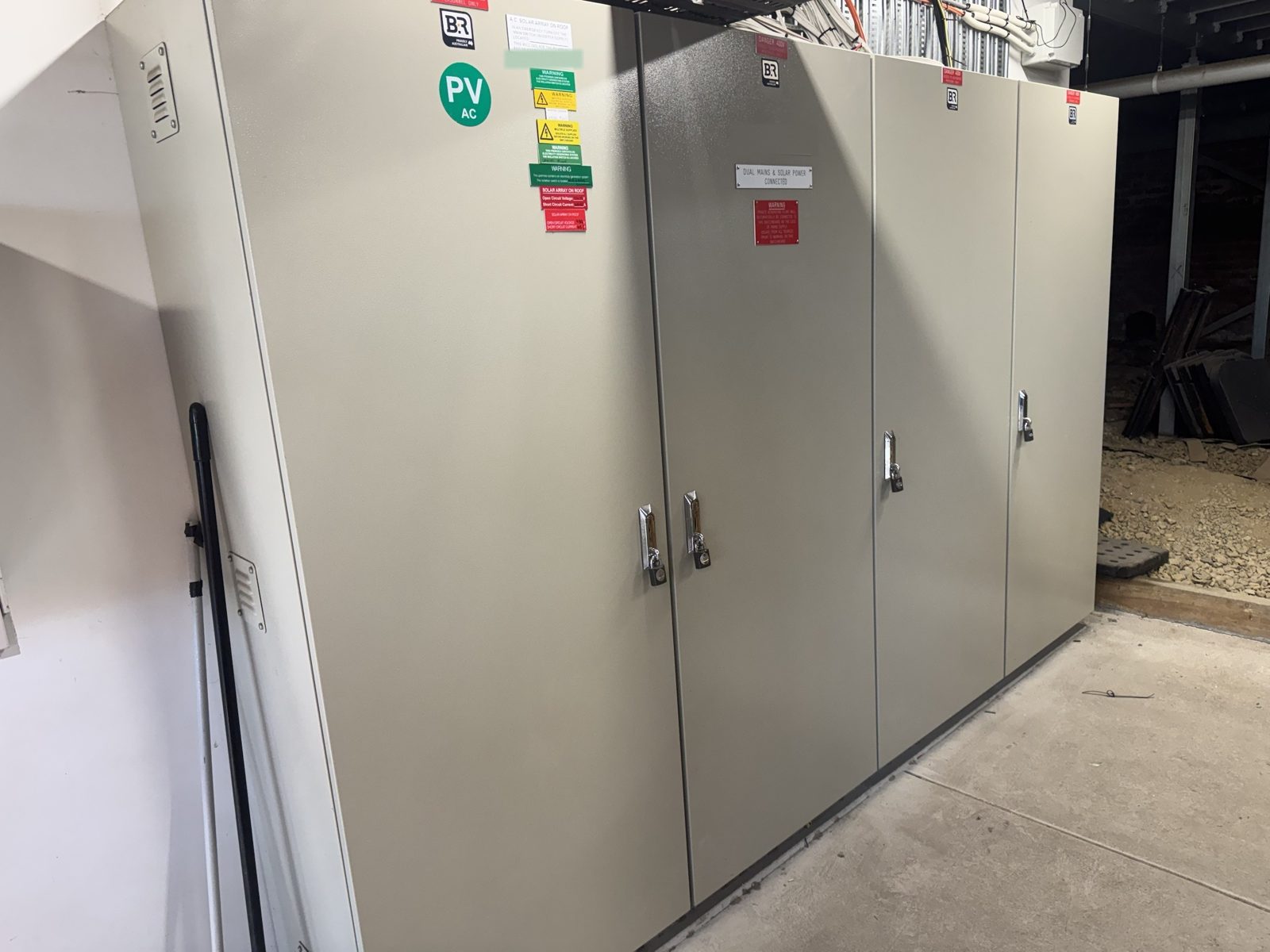 Four-door main switchboard in a switch room, doors closed and labelled, with dual mains and solar supply